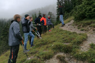 Personen stehen mit Zwickern an einem Hang, im Hintergrund Wald und Nebel